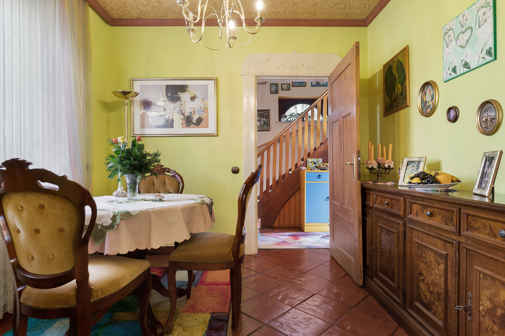 Esszimmer mit Holzmöbeln, rundem Tisch mit Blumen und Blick auf den Flur mit Treppe.