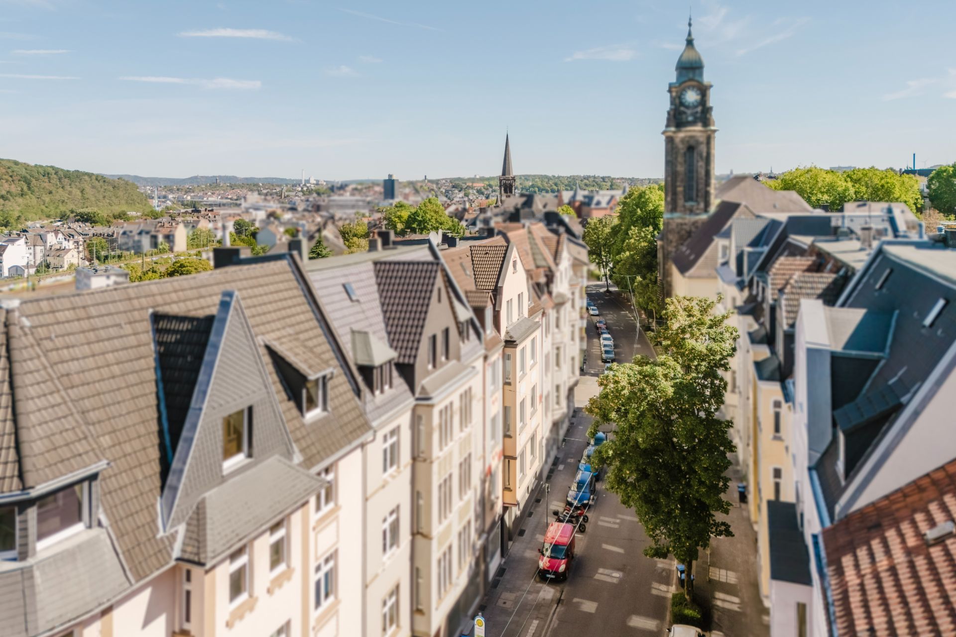 Blick auf eine Wohnstraße mit Häusern und einem Kirchturm im Hintergrund.