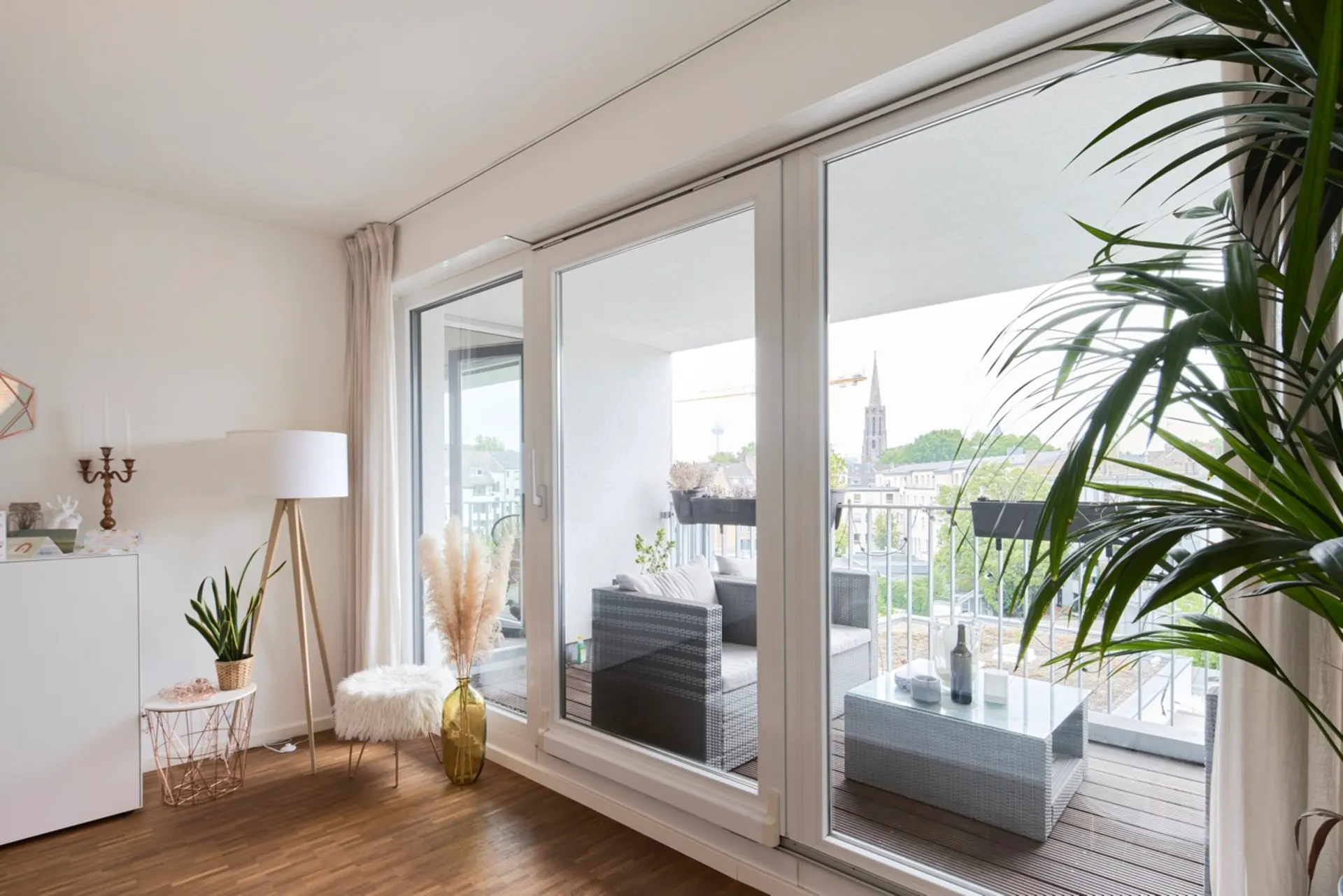 Wohnzimmer mit großen Fenstern und Zugang zu einem Balkon mit Sitzmöbeln und Tisch.