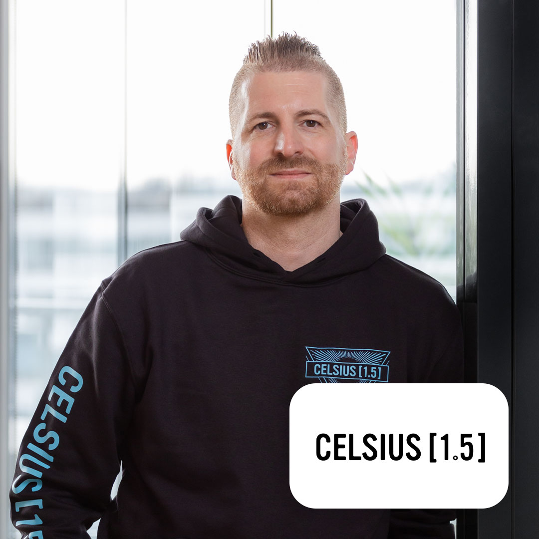 Ein Mann mit Bart trägt einen schwarzen Hoodie mit der Aufschrift 'CELSIUS [1.5]'.