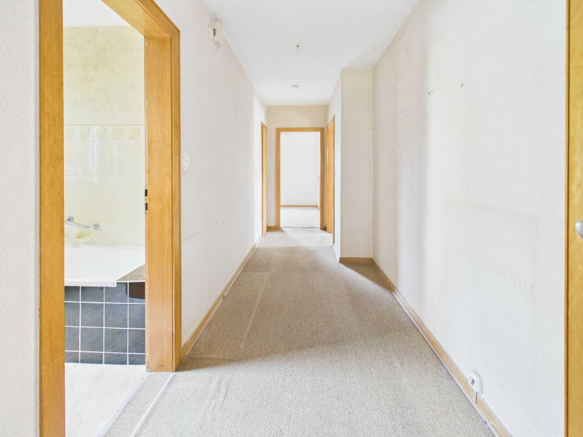 Heller Flur mit Teppichboden und mehreren offenen Türen, links ein Blick ins Badezimmer.