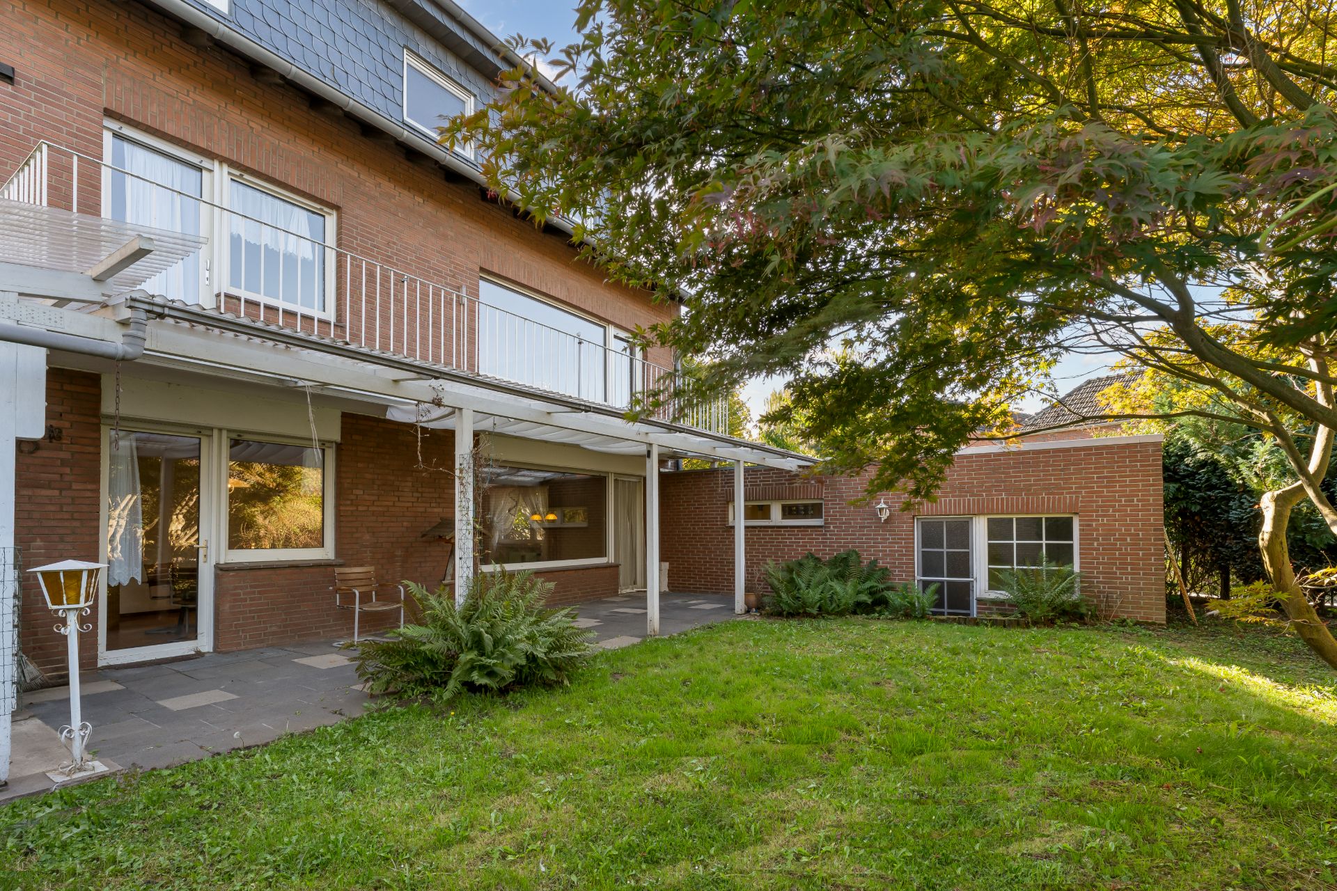 Rückseite eines Backsteinhauses mit überdachter Terrasse und Garten mit Bäumen.