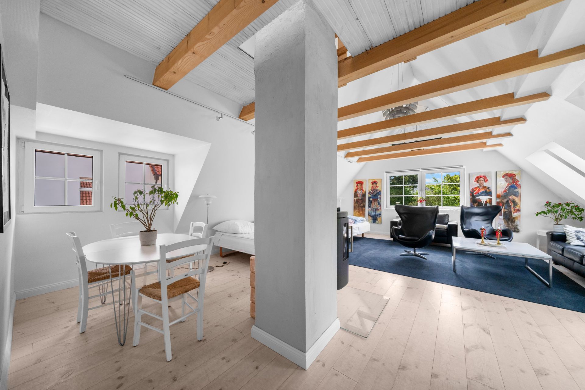 Heller Dachgeschossraum mit Essbereich, Bett, Sitzecke und sichtbaren Holzdeckenbalken.