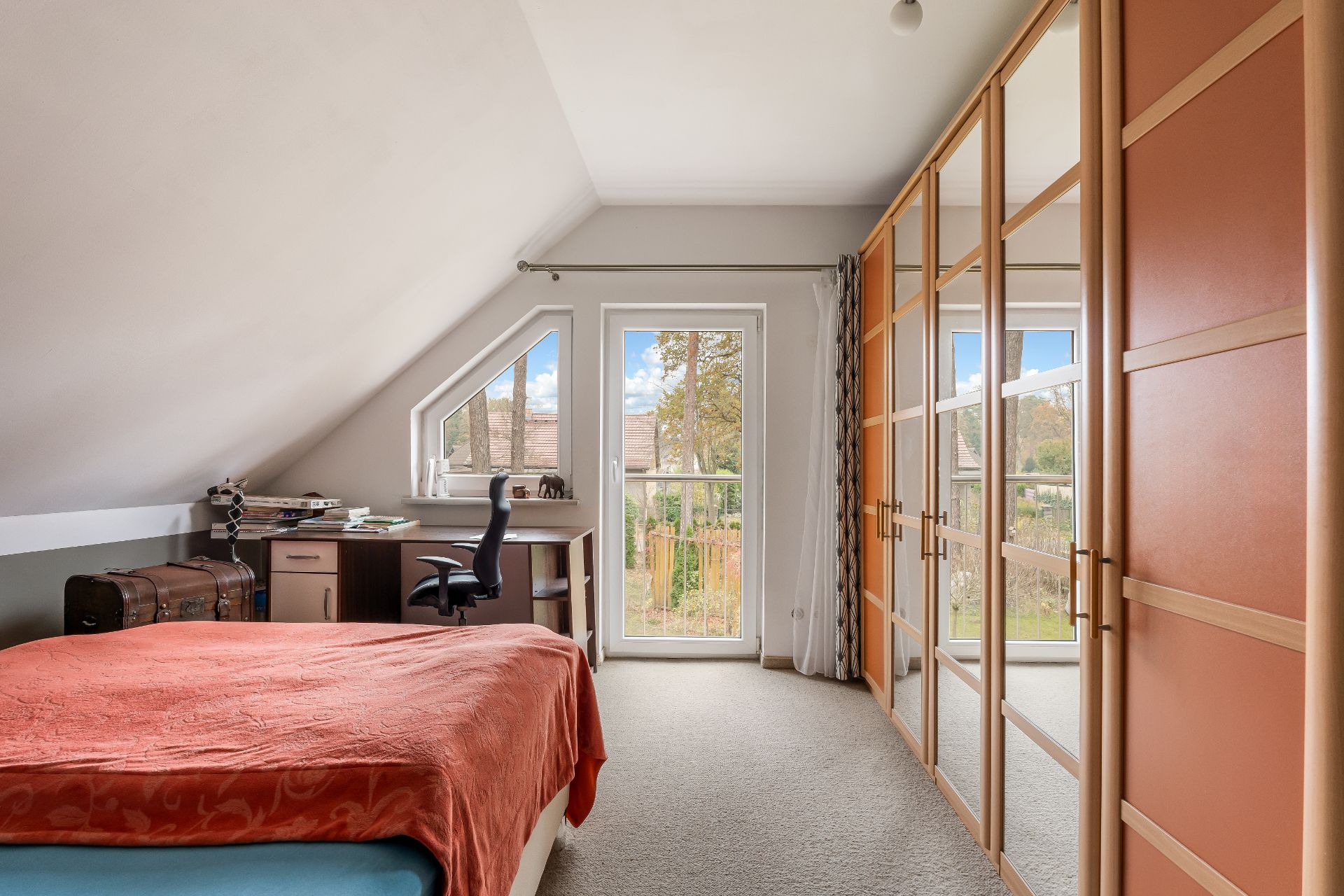 Helles Schlafzimmer mit Bett, Schreibtisch, Stuhl und großem Kleiderschrank mit Spiegel.