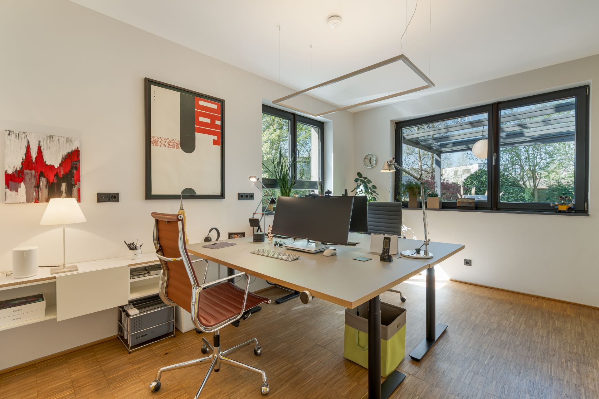 Modernes Arbeitszimmer mit großem Schreibtisch, Stuhl, Computer und großen Fenstern mit Blick ins Grüne.
