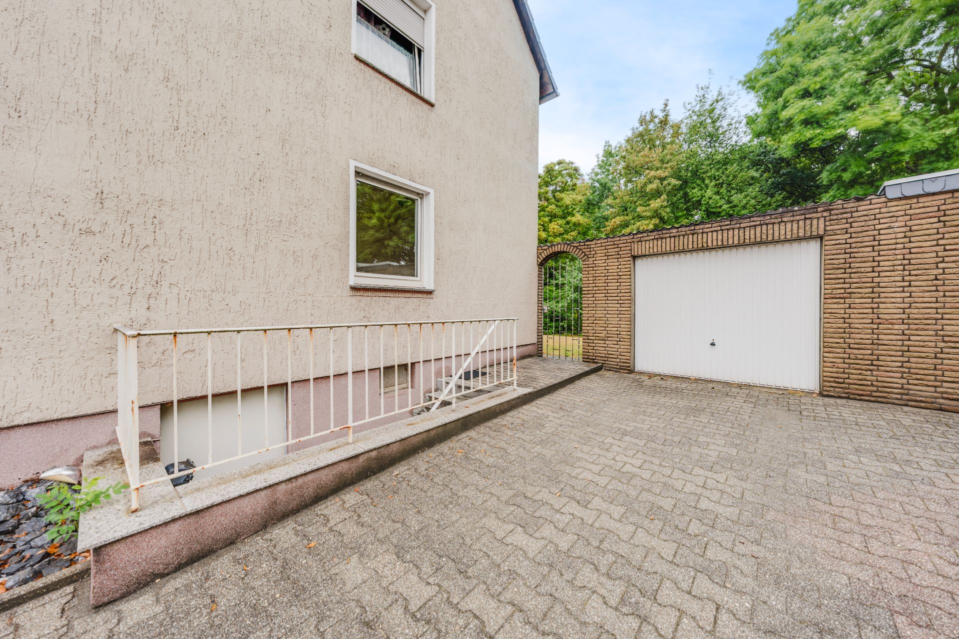 Gepflasterter Hof mit Treppe am Haus und einer geschlossenen Garage daneben.