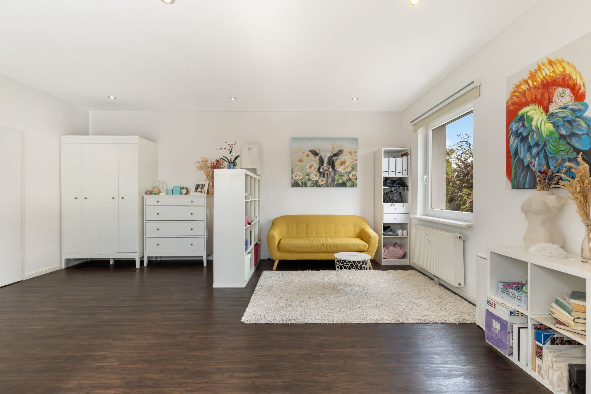 Helles Wohnzimmer mit gelbem Sofa, weißen Möbeln, Teppich und großen Fenstern.