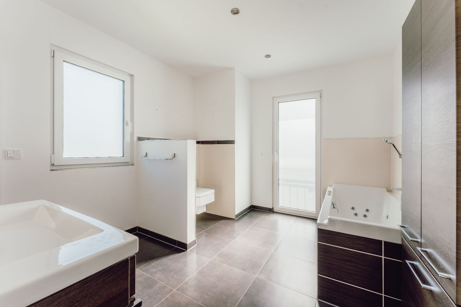 Modernes Badezimmer mit Badewanne, Waschbecken, großem Fenster und Tür zum Balkon.