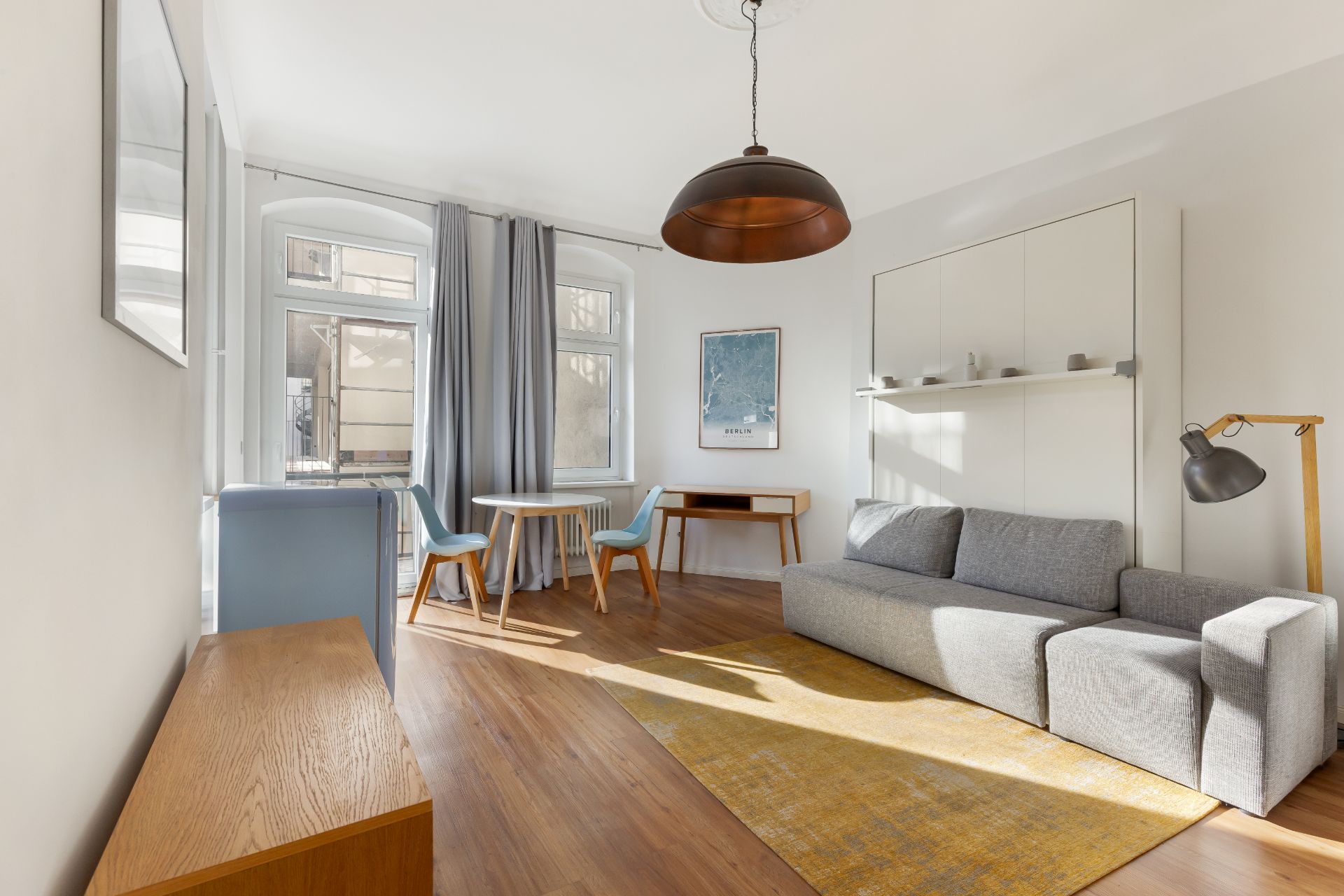 Helles Wohnzimmer mit grauem Sofa, gelbem Teppich, Tisch mit zwei Stühlen und großem Fenster.