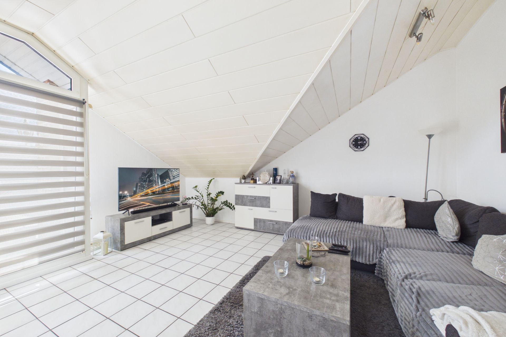 Wohnzimmer mit Ecksofa, Couchtisch, Fernseher, weißen Möbeln und Dachschräge.