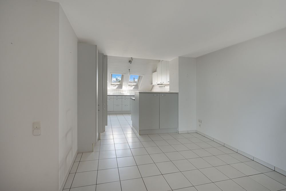 Heller Raum mit Fliesenboden, Einbauschränken und moderner Küche mit Dachfenstern.