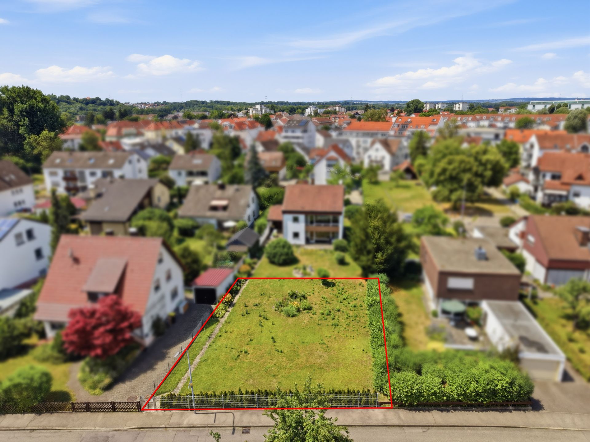 Luftaufnahme eines leeren, umzäunten Grundstücks in einem Wohngebiet mit Häusern im Hintergrund.