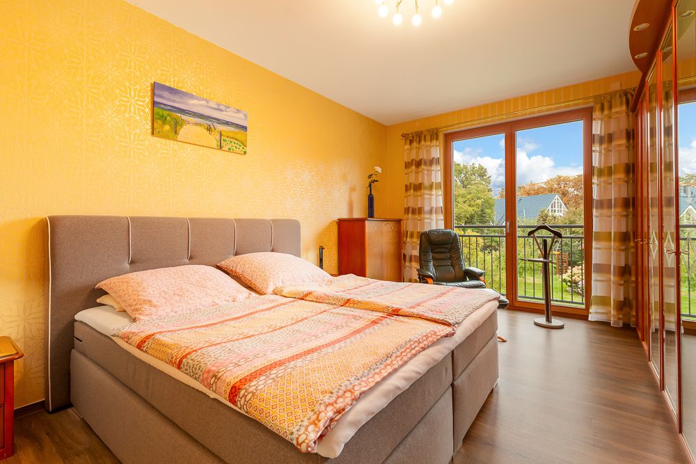 Schlafzimmer mit Doppelbett, gelber Wand, Sessel und großem Fenster mit Blick ins Grüne.