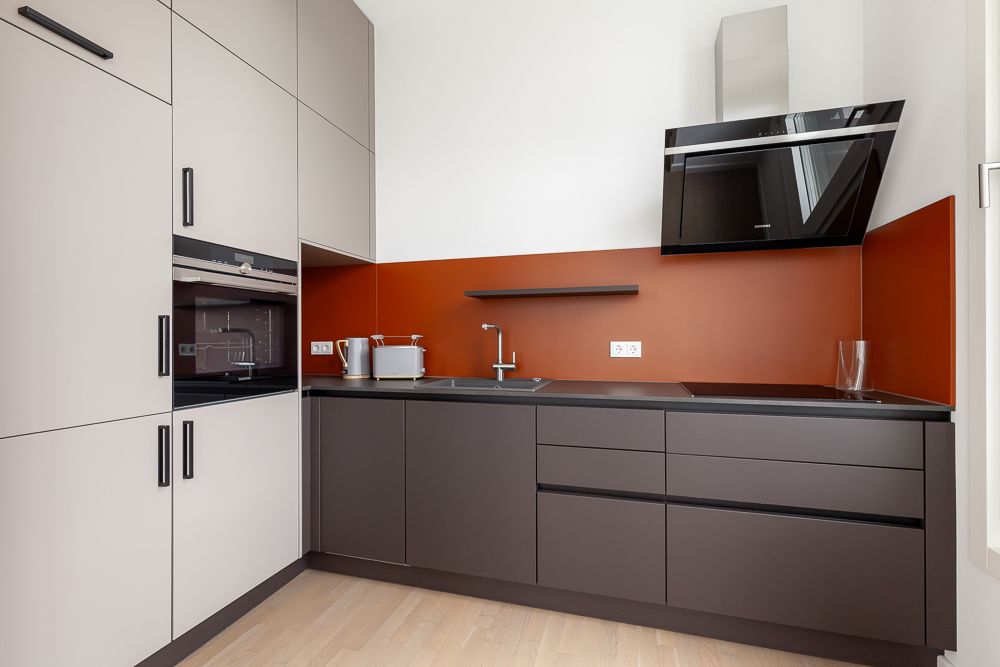 Moderne Einbauküche mit dunklen Unterschränken, roter Rückwand und Geräten.