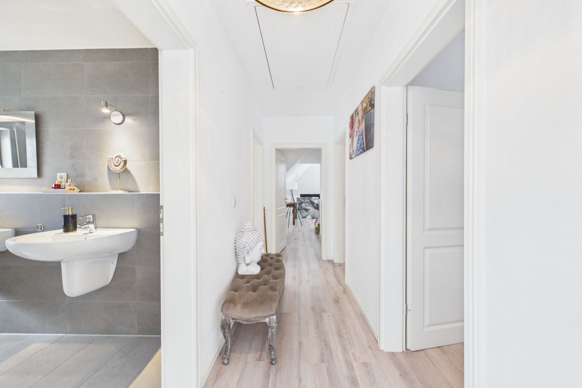 Heller Flur mit Bank, Statue und Blick ins Badezimmer mit Waschbecken.