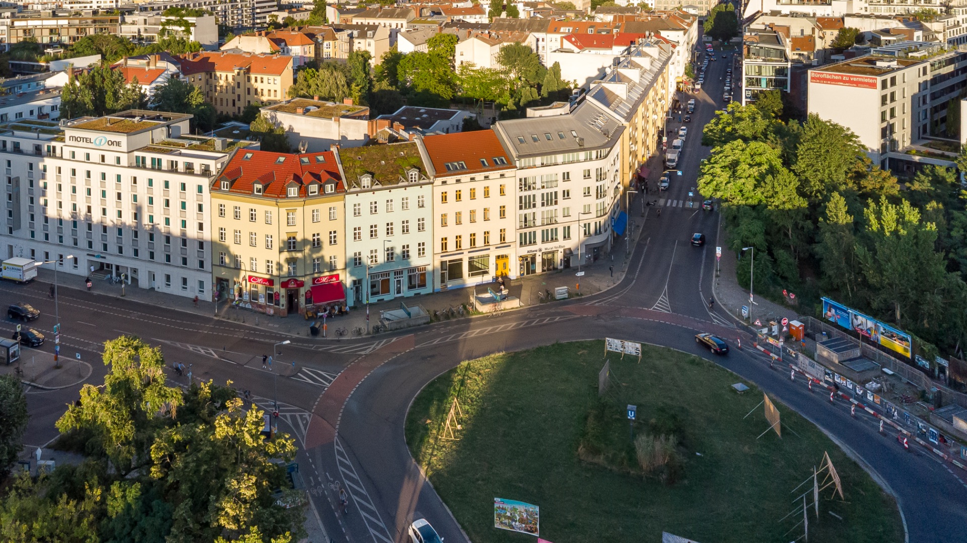 Luftaufnahme von Wohnhäusern an einer Straßenkreuzung mit grünem Kreisverkehr und umliegender Bebauung.