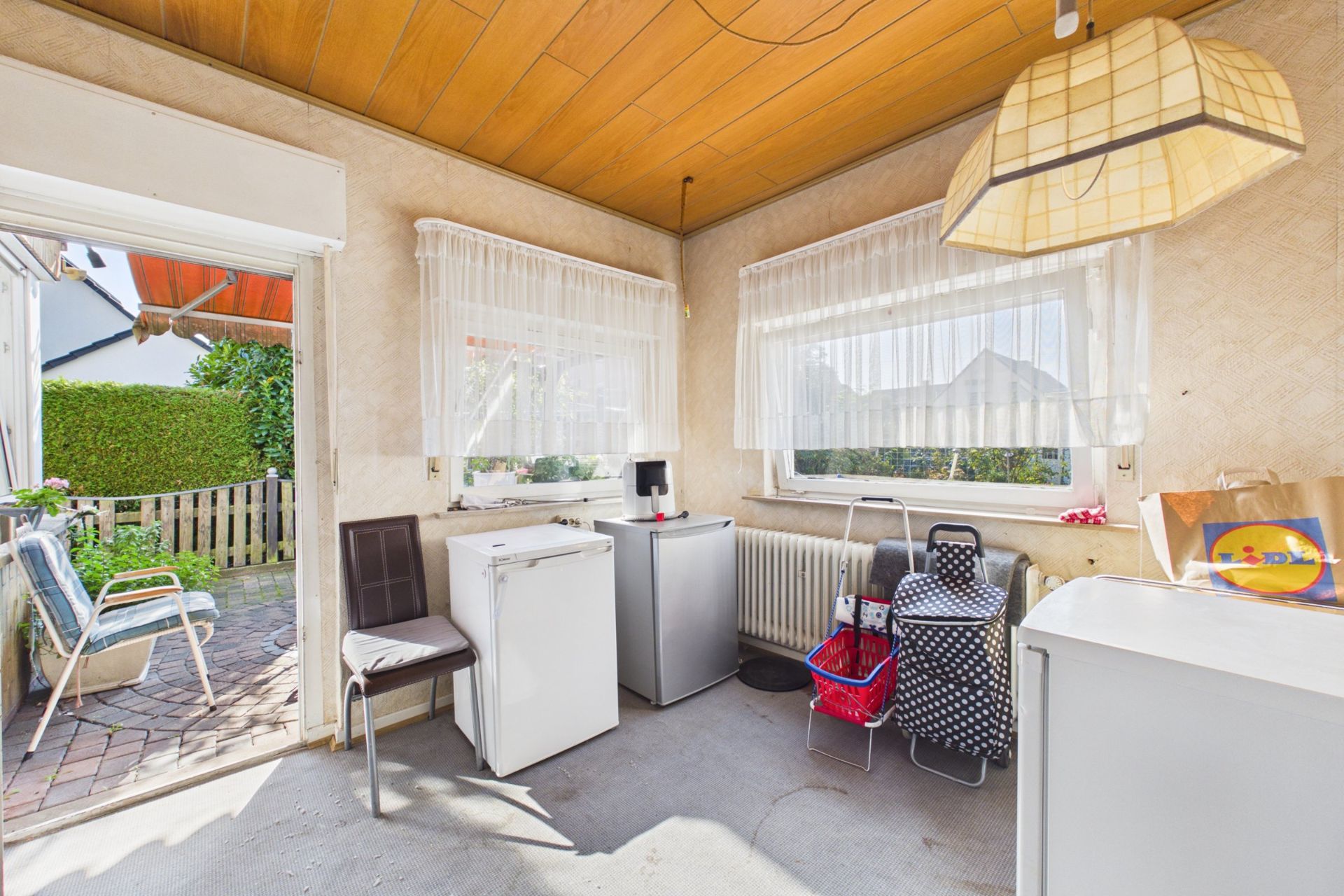 Heller Raum mit Holzbalkendecke, Kühlschränken, Stühlen und Zugang zur Terrasse.