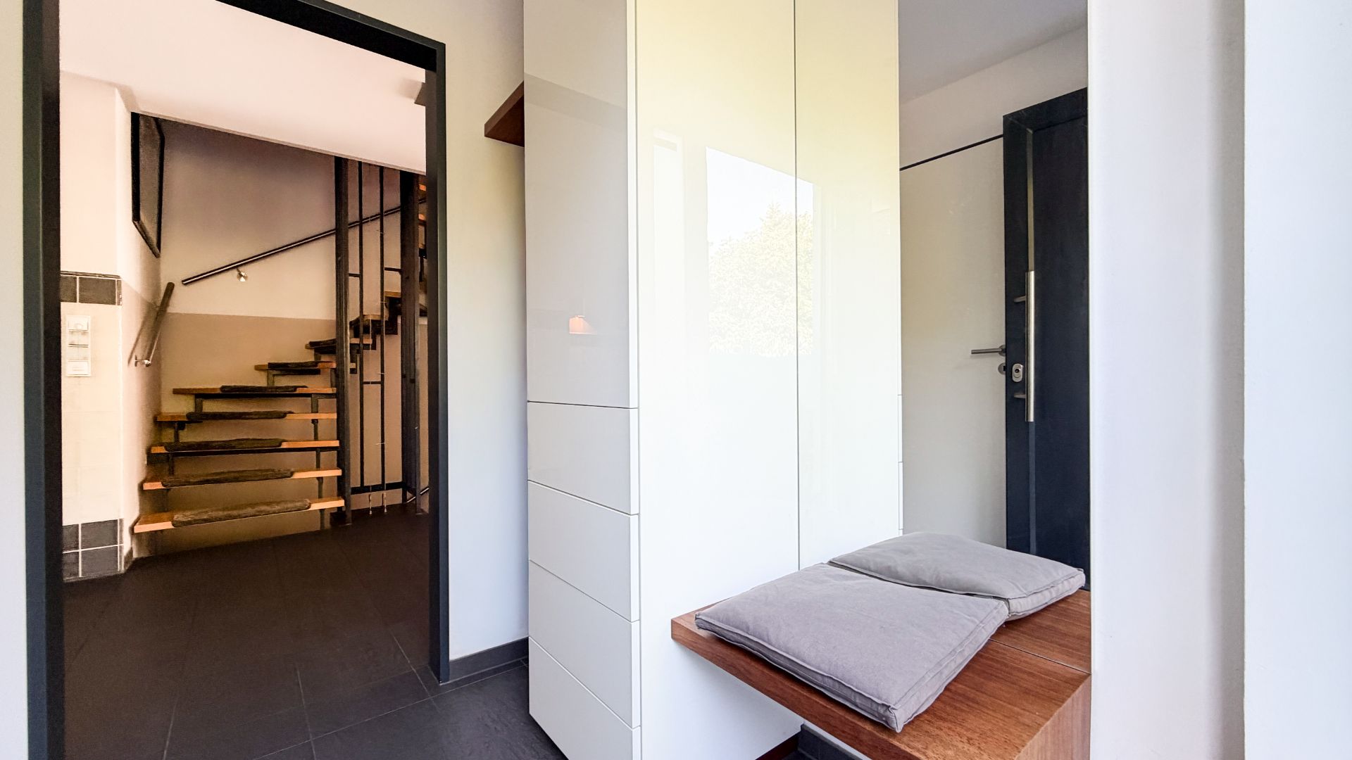 Flur mit Garderobe, Sitzbank mit Kissen und Blick auf eine offene Holztreppe.