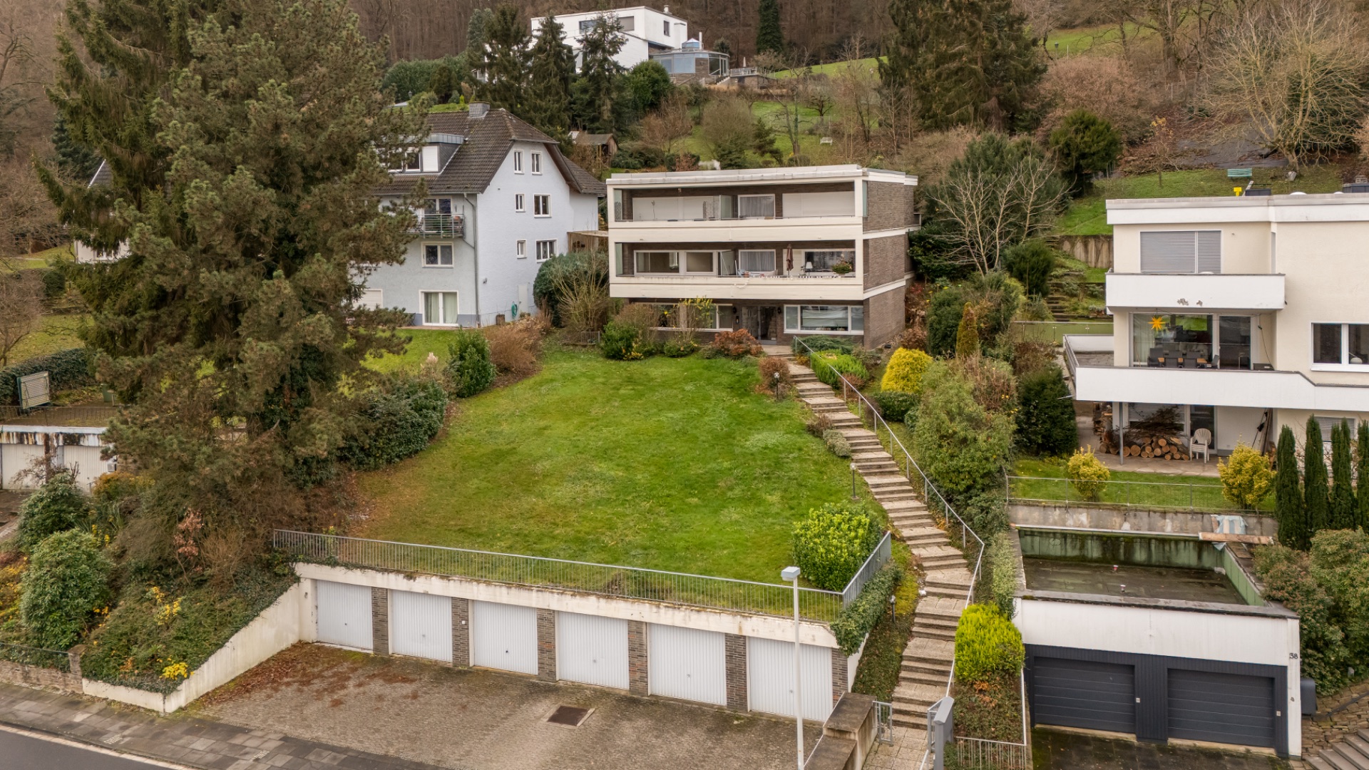 Zwei Wohnhäuser mit großen Fenstern, einem Garten und mehreren Garagen im Vordergrund.