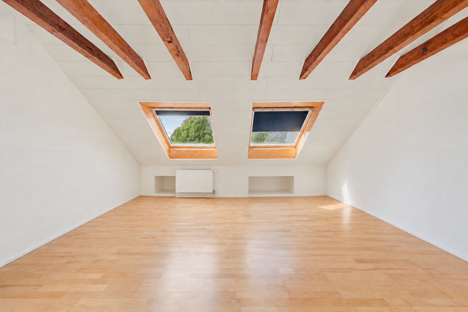 Dachzimmer mit Holzfußboden, sichtbaren Holzbalken und zwei großen Dachfenstern.