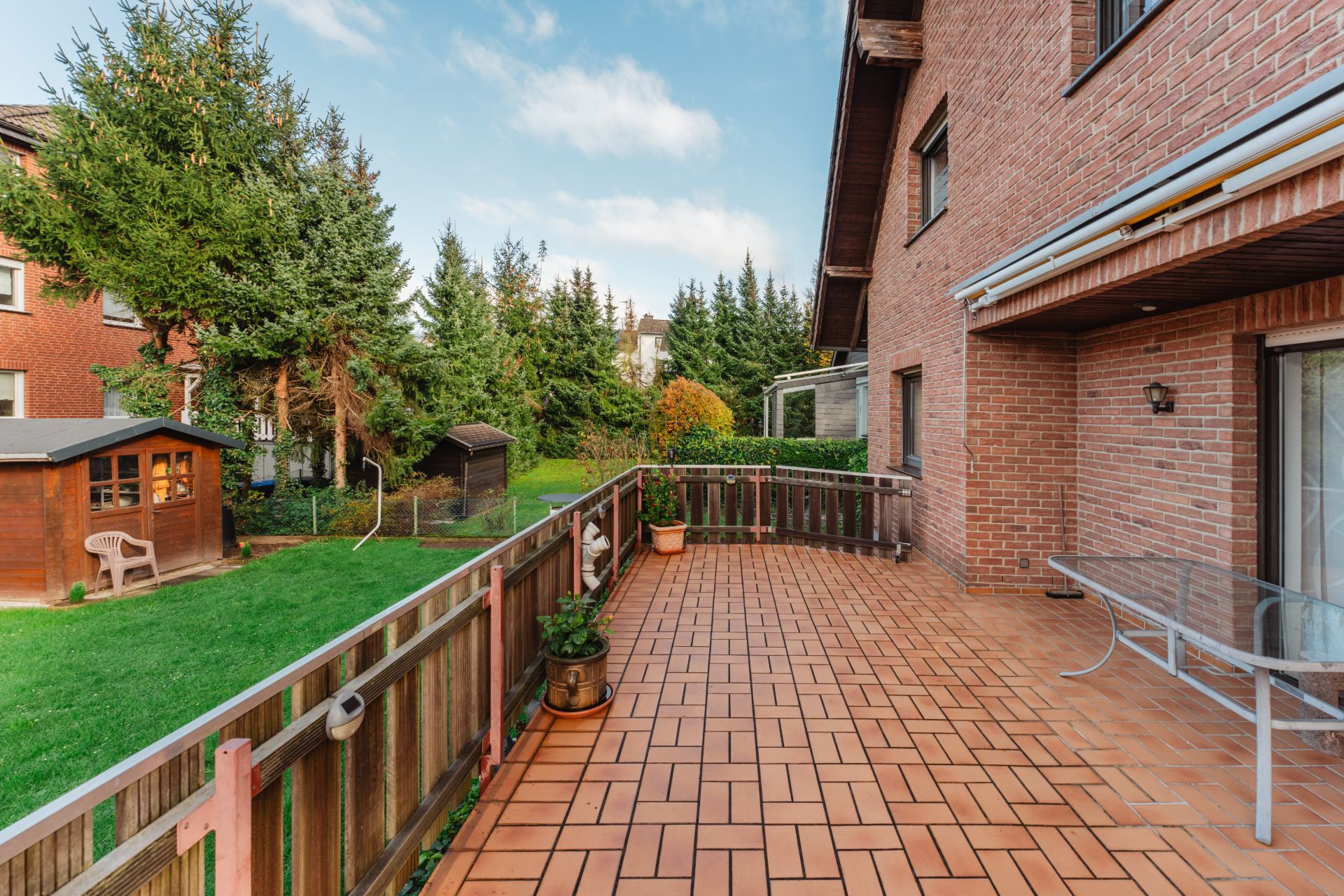 Große Terrasse mit Fliesenboden und Holzzaun neben einem Garten mit zwei Holzhütten.