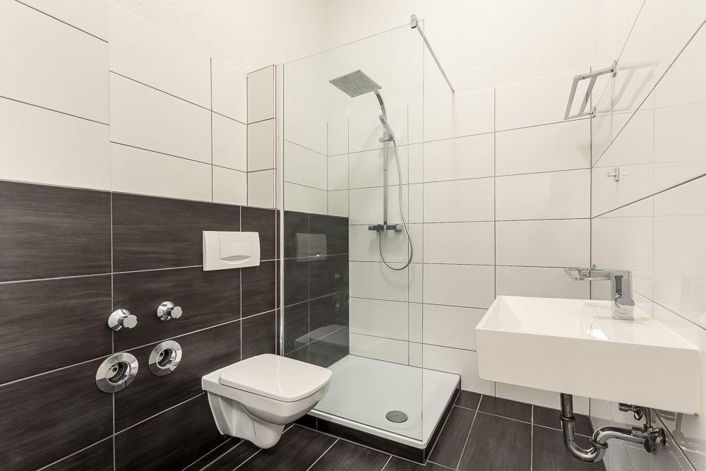 Modernes Badezimmer mit Dusche, Wand-WC und Waschbecken, weiße und dunkle Fliesen.