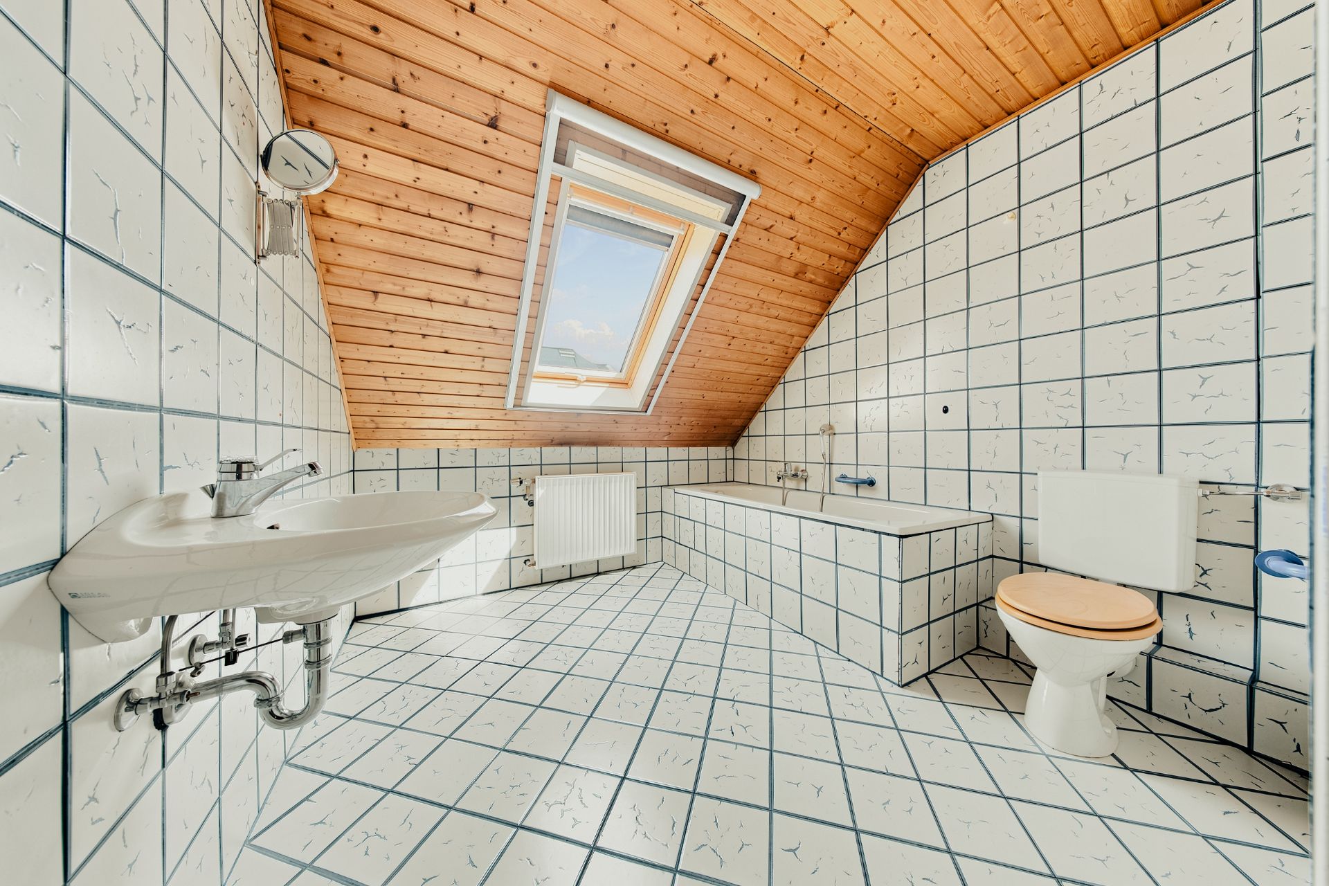 Helles Bad mit Dachschräge, Fliesen, Fenster, Wanne, Waschbecken und WC.
