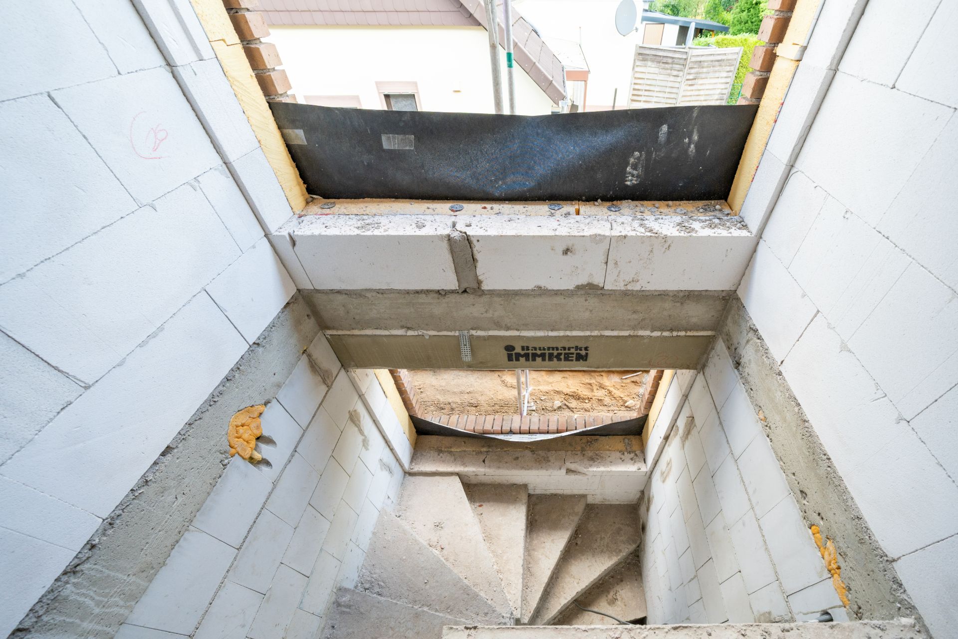 Unfertiger Treppenabgang in einem Rohbau mit weißen Wänden und Baustellenmaterial.
