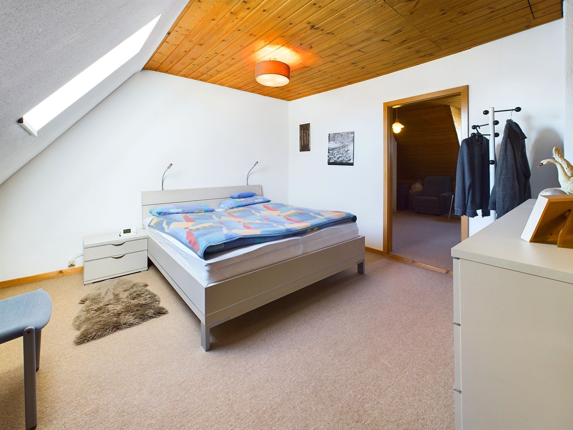 Helles Schlafzimmer mit Doppelbett, Nachttisch, Teppich und Dachschräge.