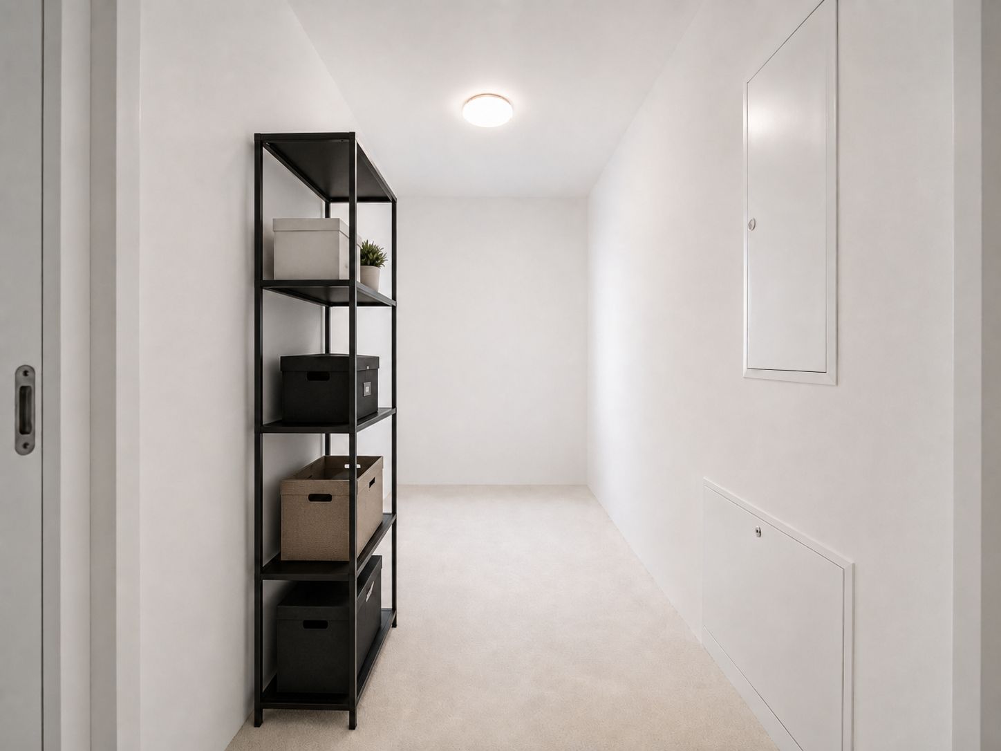 Schmaler, heller Flur mit schwarzem Regal und Aufbewahrungsboxen an der linken Wand.