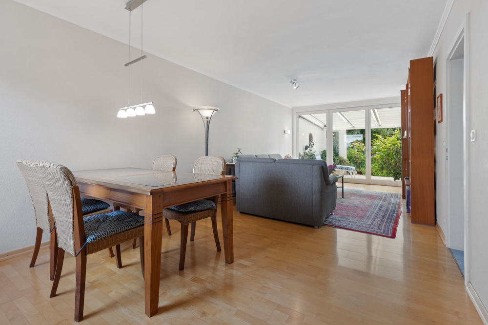 Wohnzimmer mit Essbereich, Holzboden, Esstisch, Sofas und Blick auf Terrasse mit Garten.