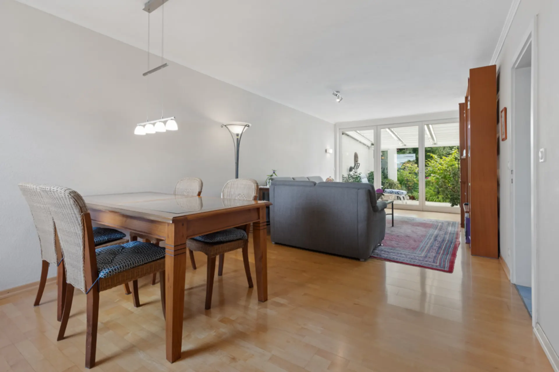 Wohnzimmer mit Essbereich, Holzboden, Esstisch, Sofas und Blick auf Terrasse mit Garten.