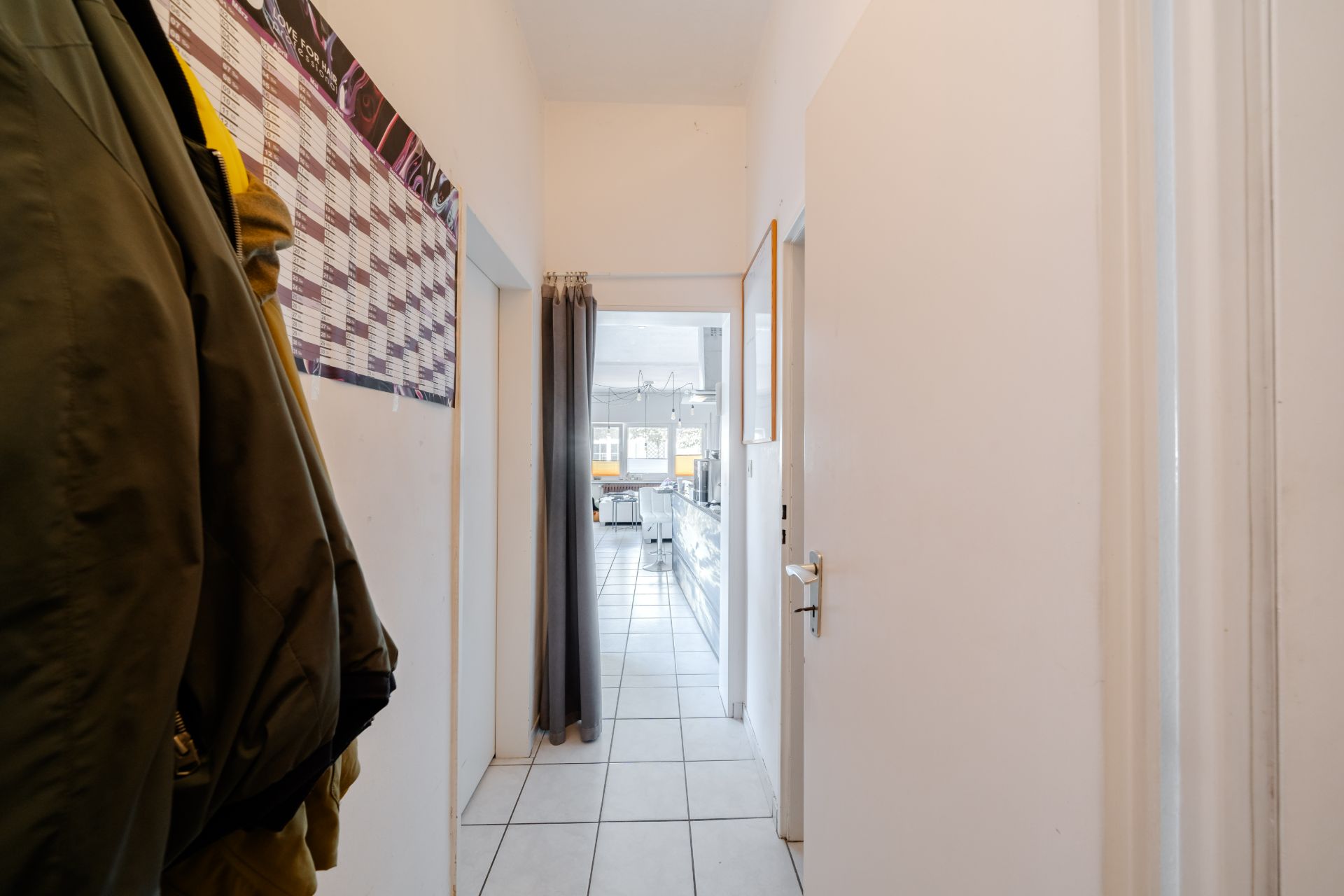 Schmaler Flur mit weißem Fliesenboden, Garderobe links und Blick in eine helle Küche.