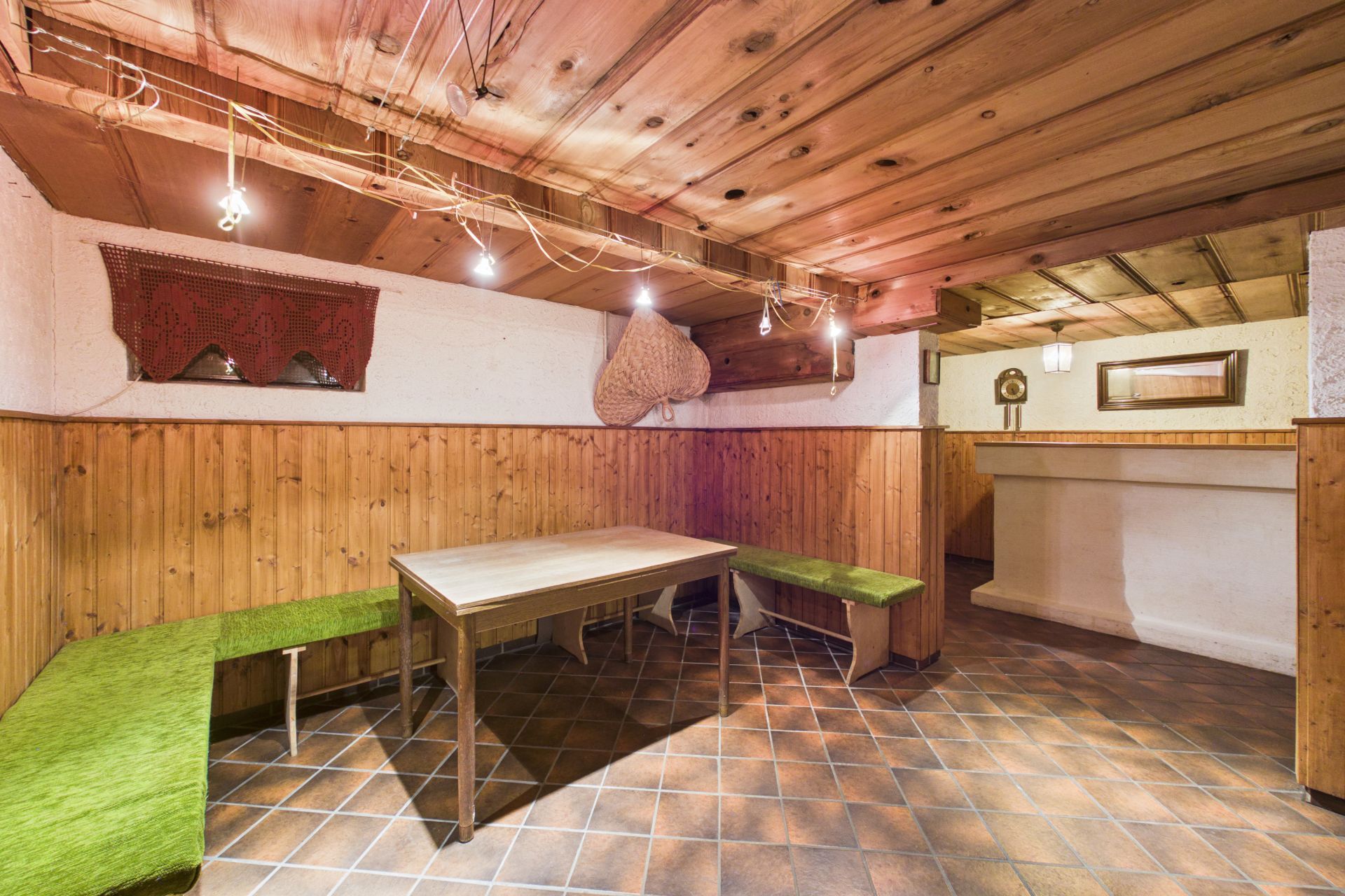 Rustikaler Raum mit Holzwand, Holzbänken, Holztisch und gekacheltem Boden.