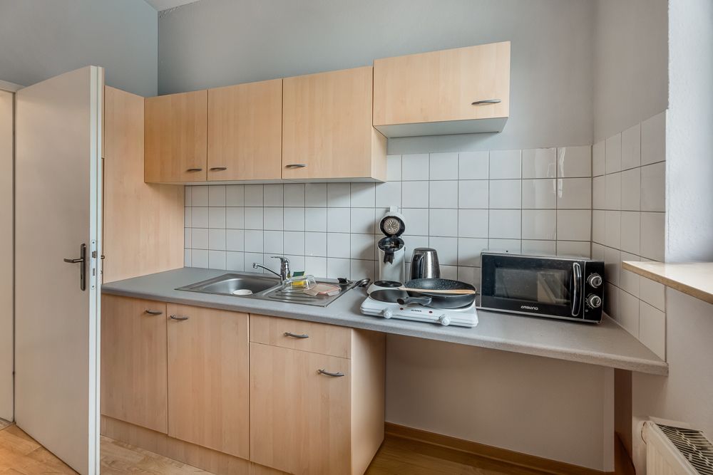 Kleine Küche mit Holzschränken, Spüle, Kochplatte, Mikrowelle und Kaffeemaschine.