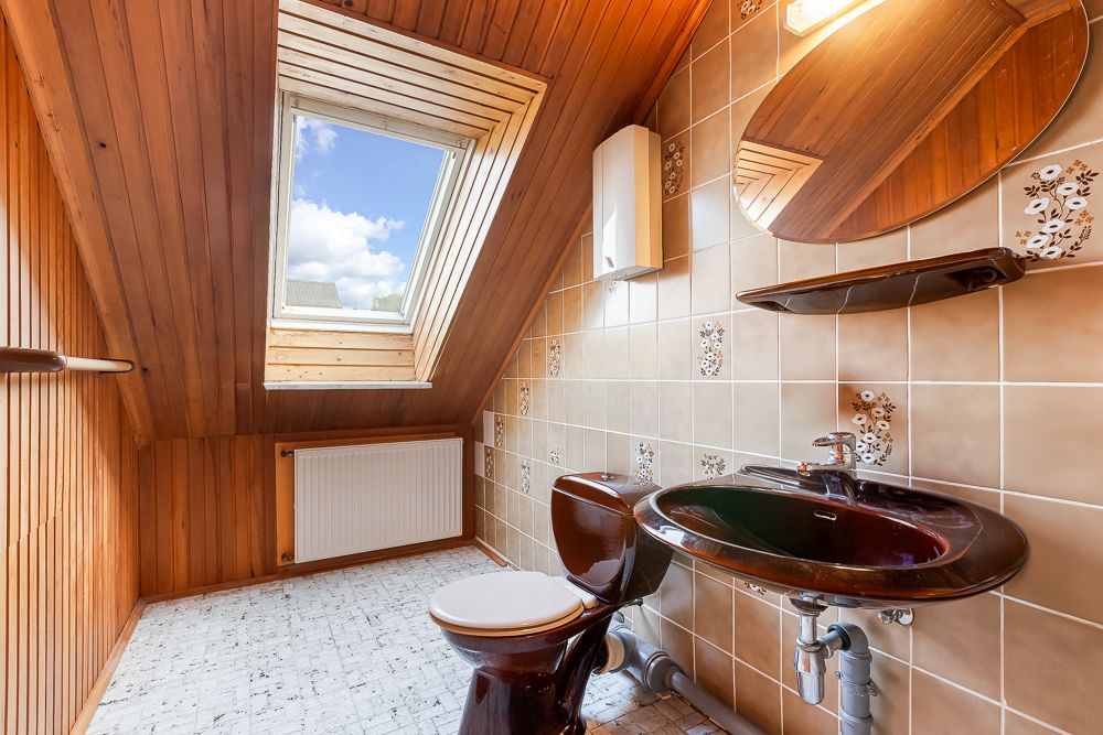 Dachgeschoss-Badezimmer mit Dachfenster, brauner Toilette und Waschbecken, Holzdecke und beigen Fliesen.