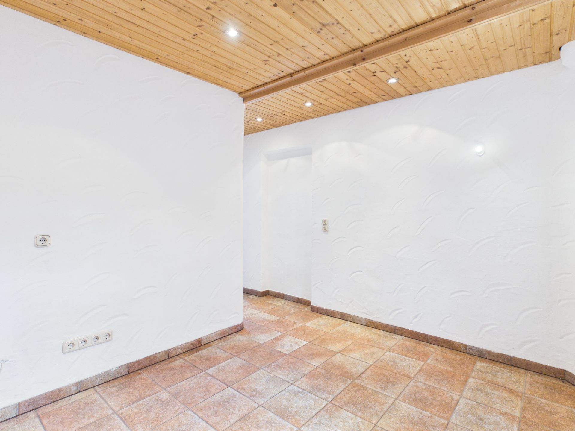 Leerer Raum mit weißen Wänden, Fliesenboden und Holzdecke mit Einbauleuchten.