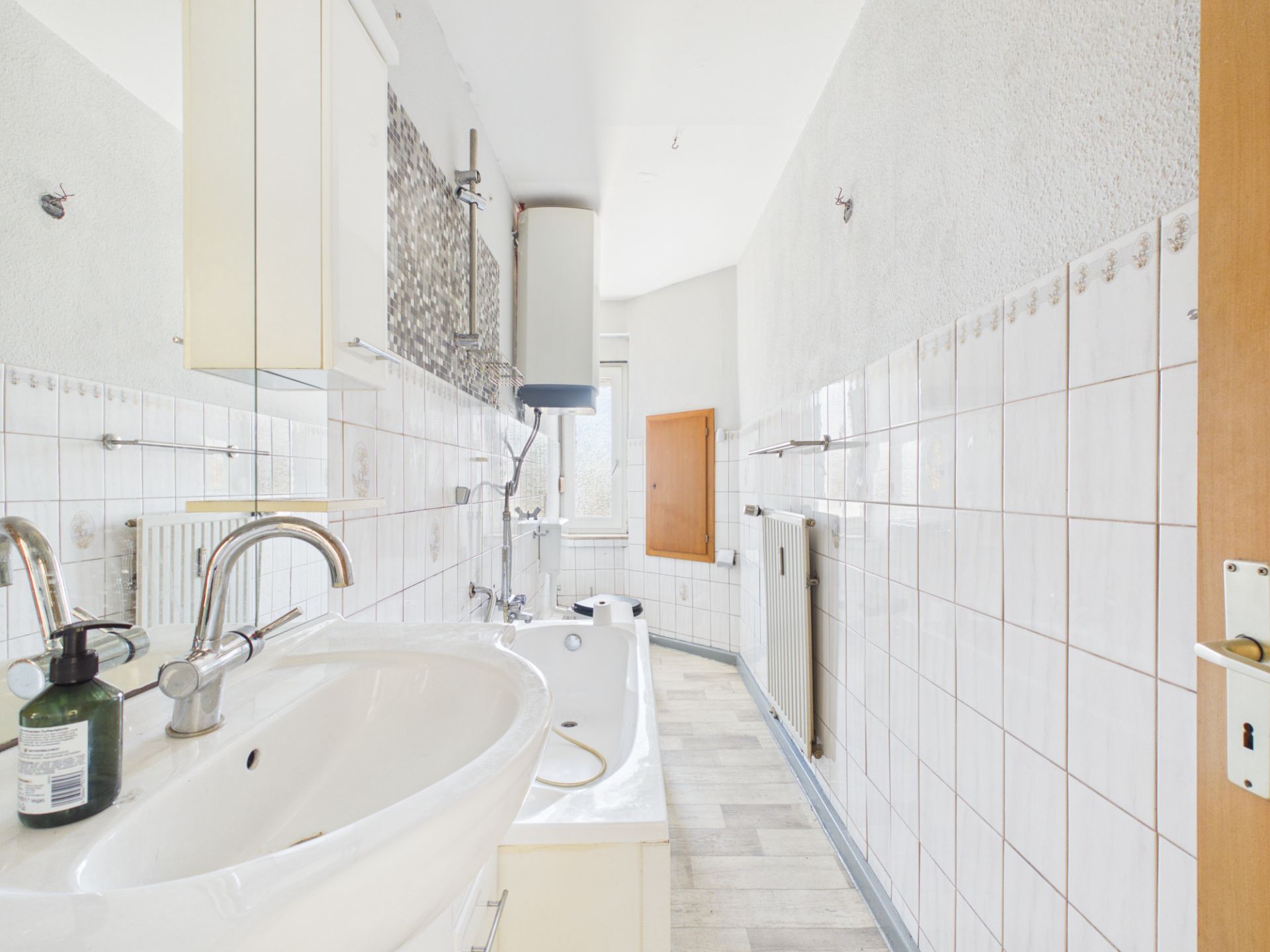 Helles Badezimmer mit Waschbecken, Badewanne, weißen Fliesen und Fenster am Ende des Raums.