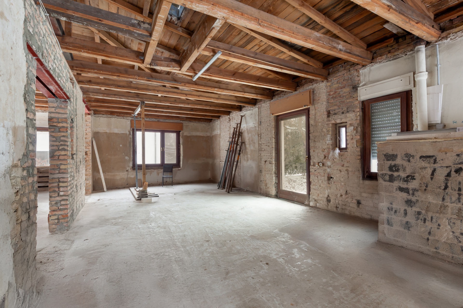 Leerer Raum mit sichtbaren Holzbalken an der Decke und Rohbauwänden.