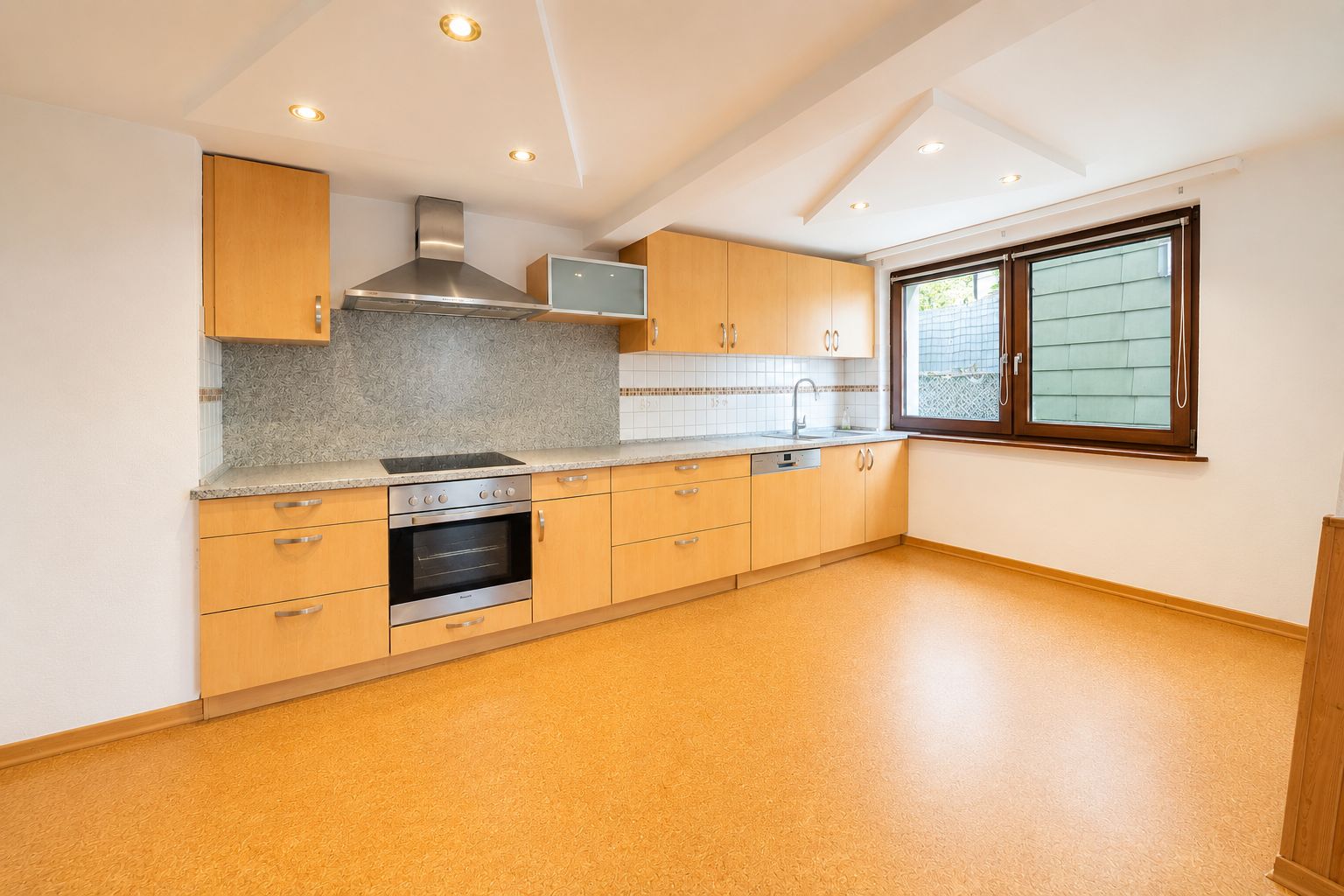 Moderne Einbauküche mit Holzschränken, Herd, Ofen, Spüle und großem Fenster.