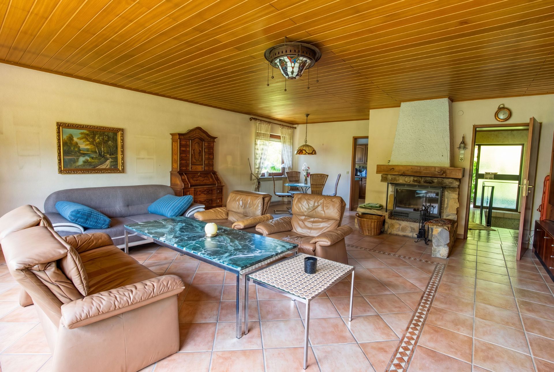 Wohnzimmer mit Ledersesseln, Couch, Kamin, Marmortisch und Fliesenboden.