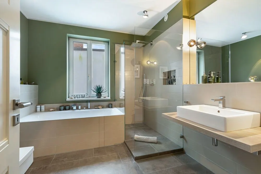 Modernes Badezimmer mit Badewanne, großer Dusche und Waschbecken, grüne Wände und Fenster.