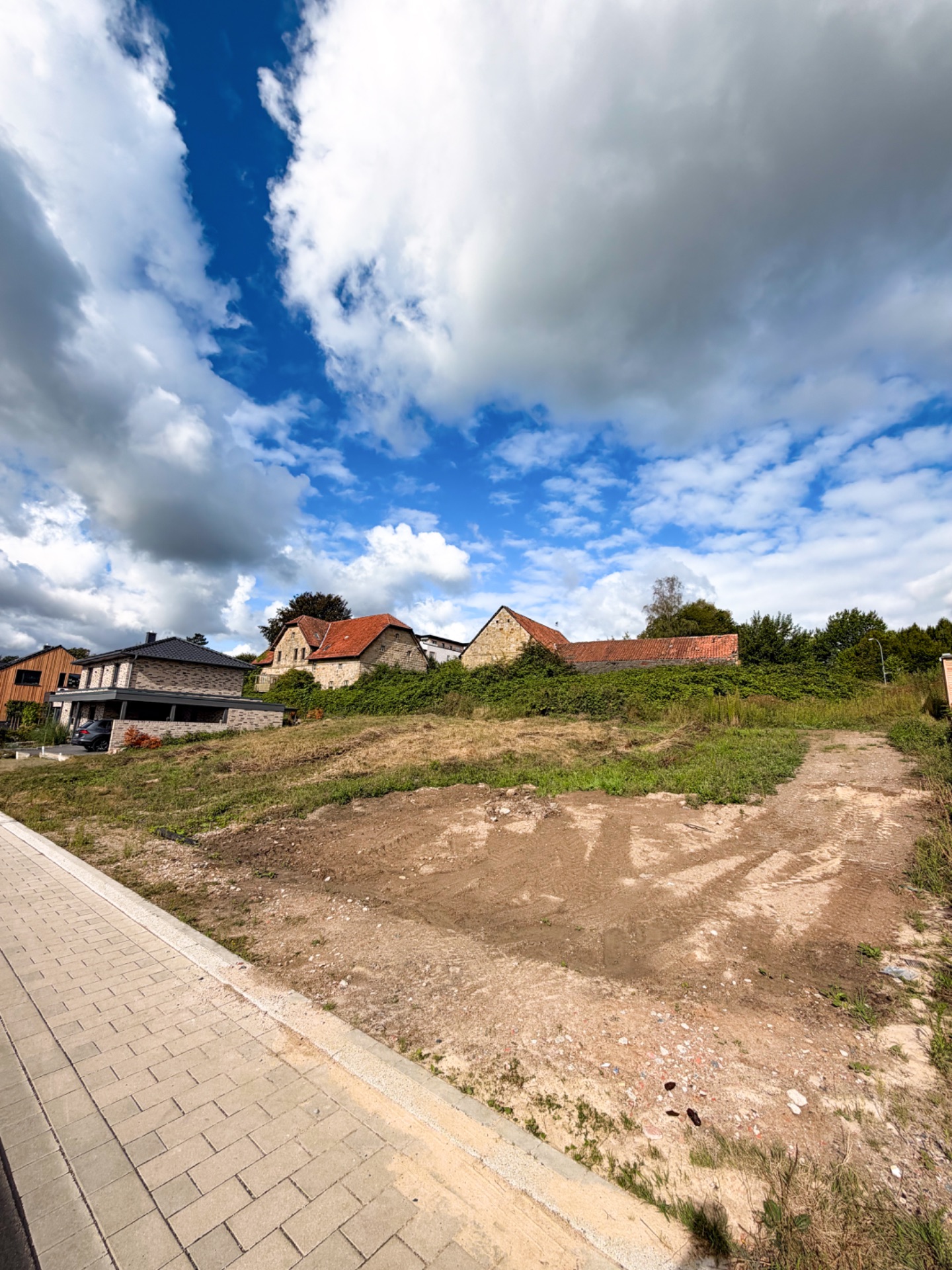 Unbebautes Grundstück an einer gepflasterten Straße mit angrenzenden Wohnhäusern im Hintergrund.