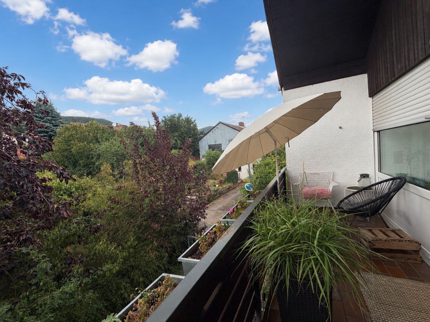 Balkon mit Stuhl, Sonnenschirm, Pflanze und Blick auf Bäume und Wohnhäuser.