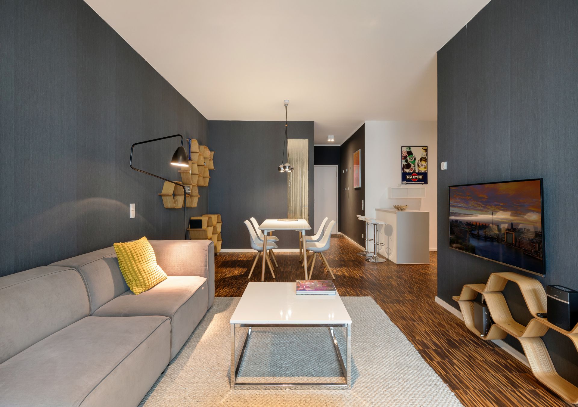 Modernes Wohnzimmer mit grauem Sofa, Couchtisch, Esstisch und Wandregalen.