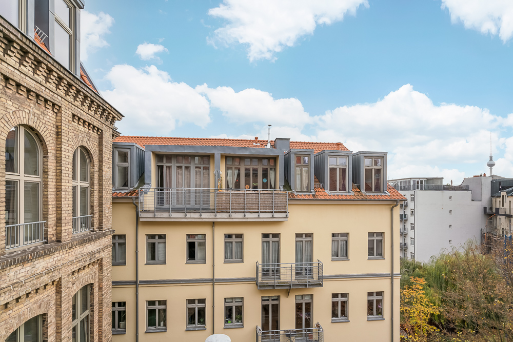 Blick auf ein gelbes Wohngebäude mit Balkonen und roten Dachziegeln bei Tageslicht.