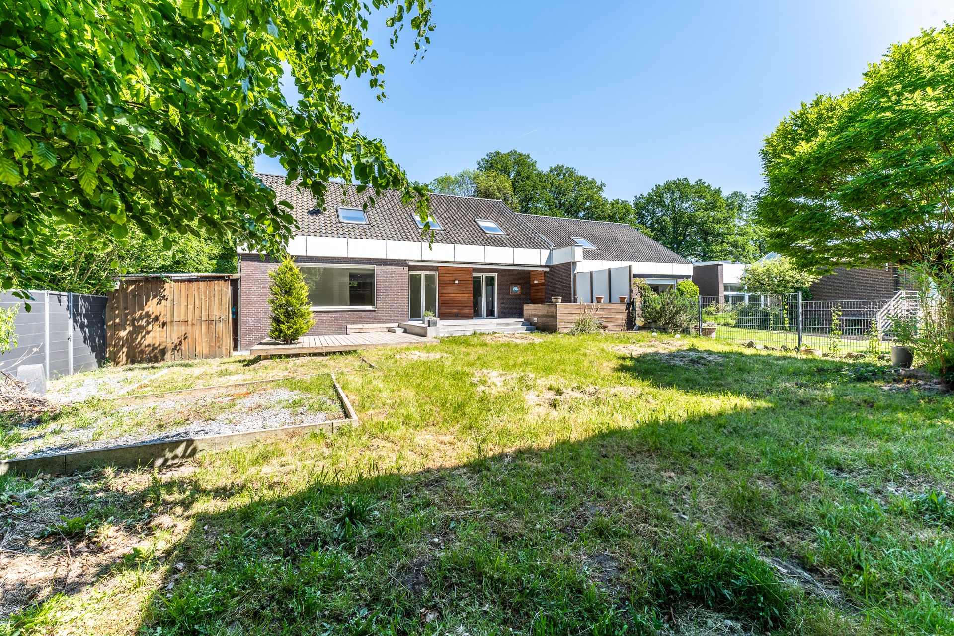 Garten mit Rasenfläche und Terrasse hinter einem modernen Wohnhaus bei sonnigem Wetter.