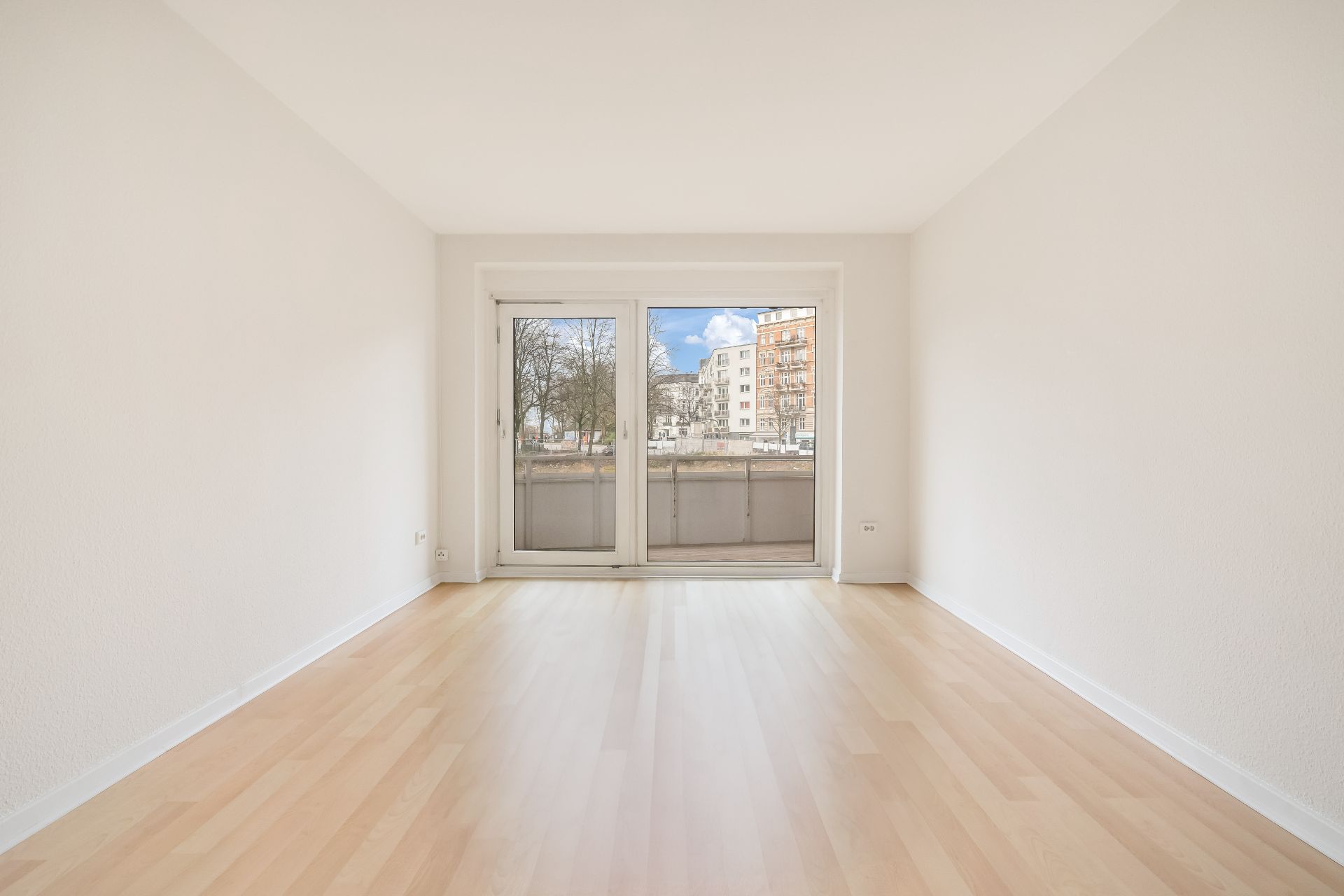 Leerer, heller Raum mit Parkettboden und großer Glas-Tür zu einem Balkon.