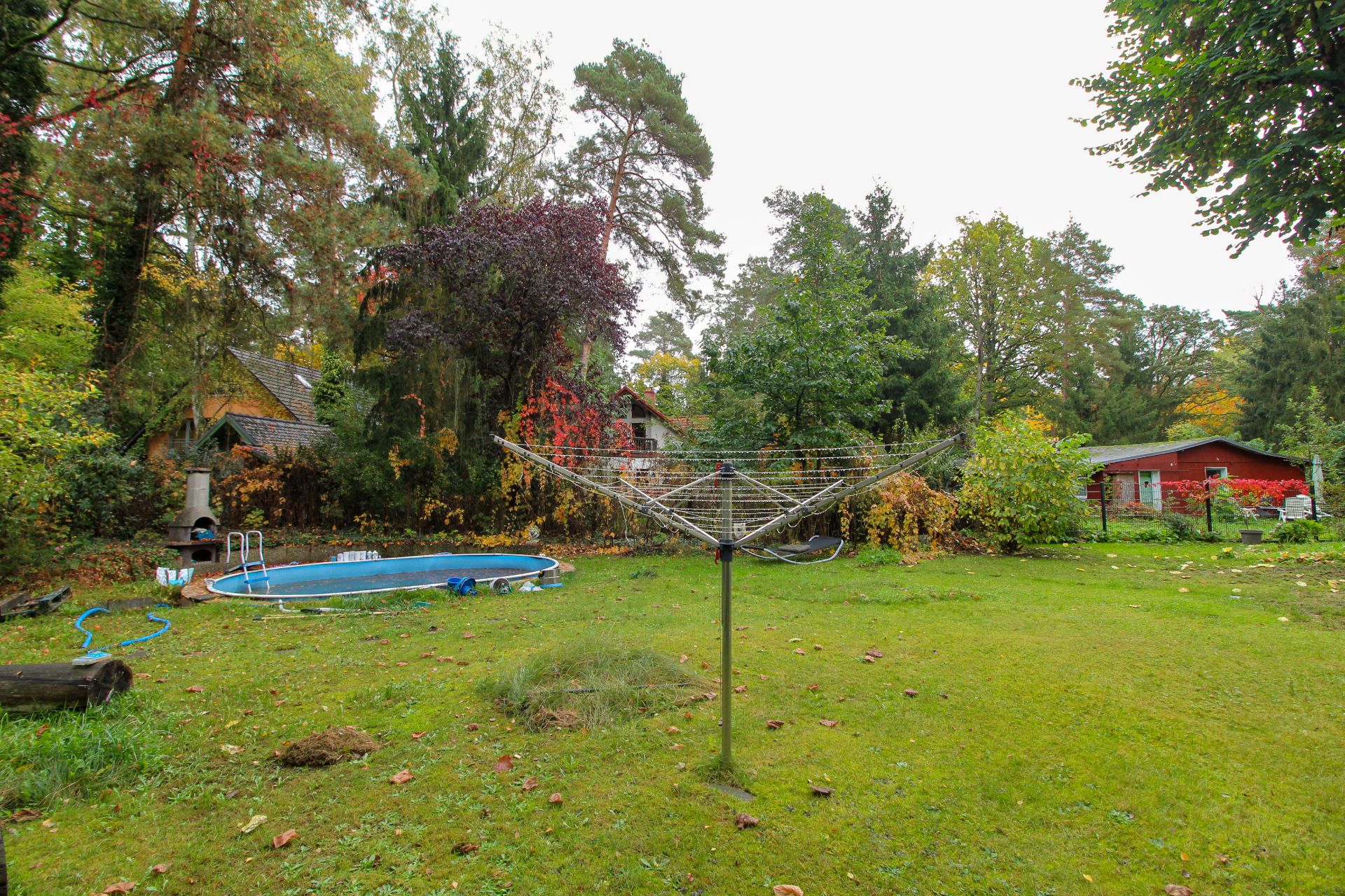 Garten mit Wäscheleine, rundem Pool und Bäumen, im Hintergrund ein rotes Haus.