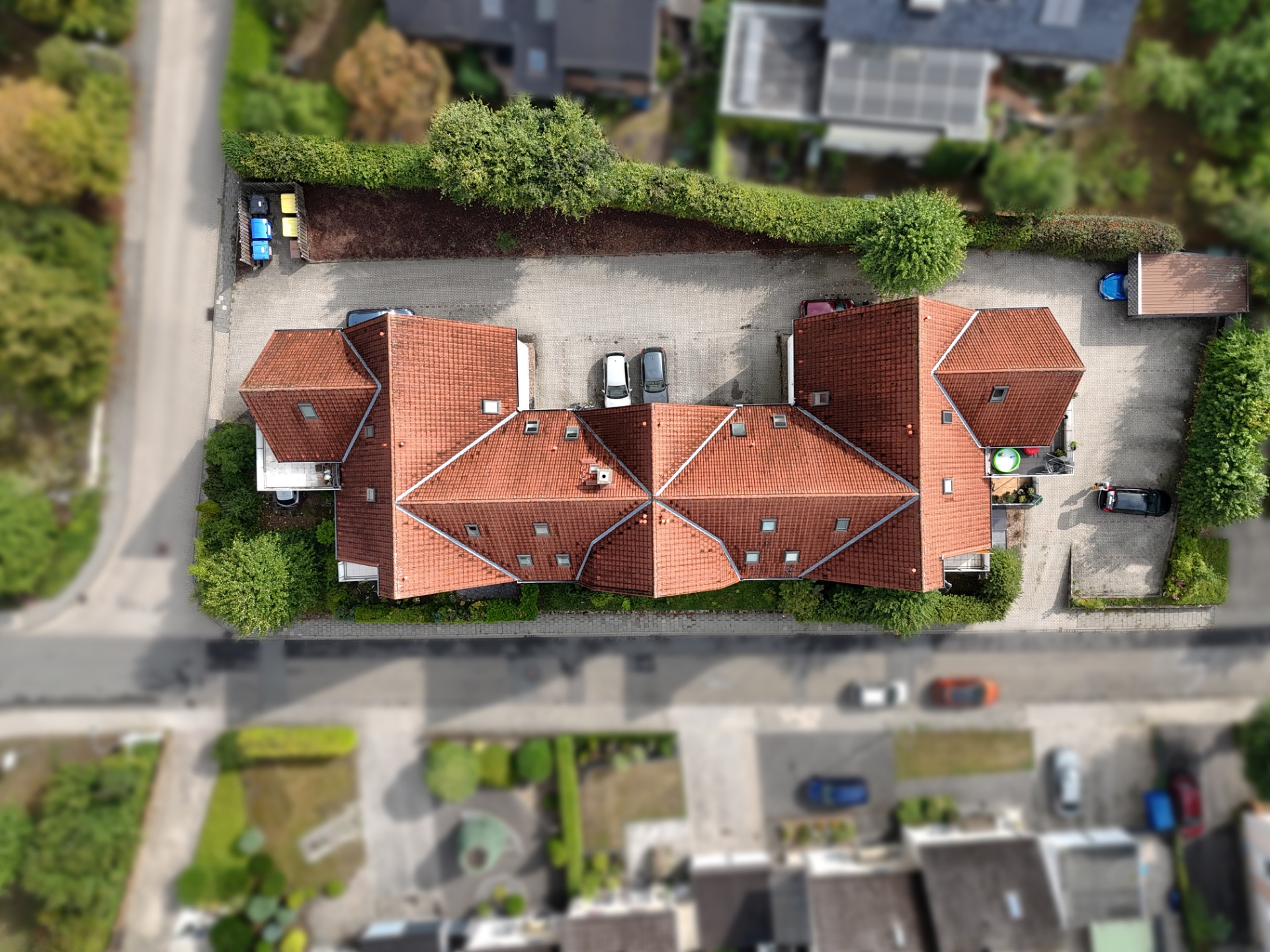 Luftaufnahme eines Wohnhauses mit rotem Dach und mehreren geparkten Autos drumherum.
